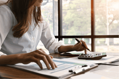 A woman in a white blouse uses a calculator over charts and graphs.